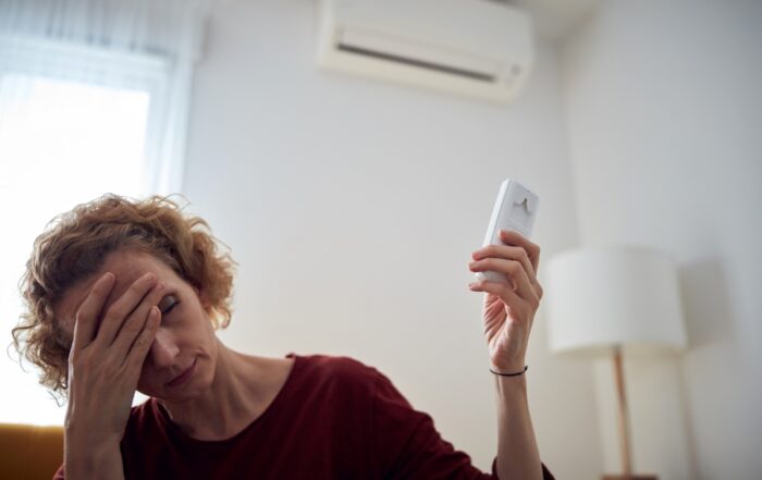 Pittsburgh homeowner frustrated with a broken air conditioner, holding her AC remote while sitting on her couch in the summer heat