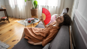 Pittsburgh homeowner lying on her couch fanning herself with a handheld fan because her air conditioner is not cooling her home effectively.