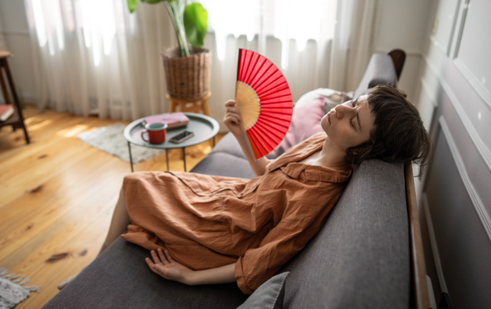 Pittsburgh homeowner lying on her couch fanning herself with a handheld fan because her air conditioner is not cooling her home effectively.